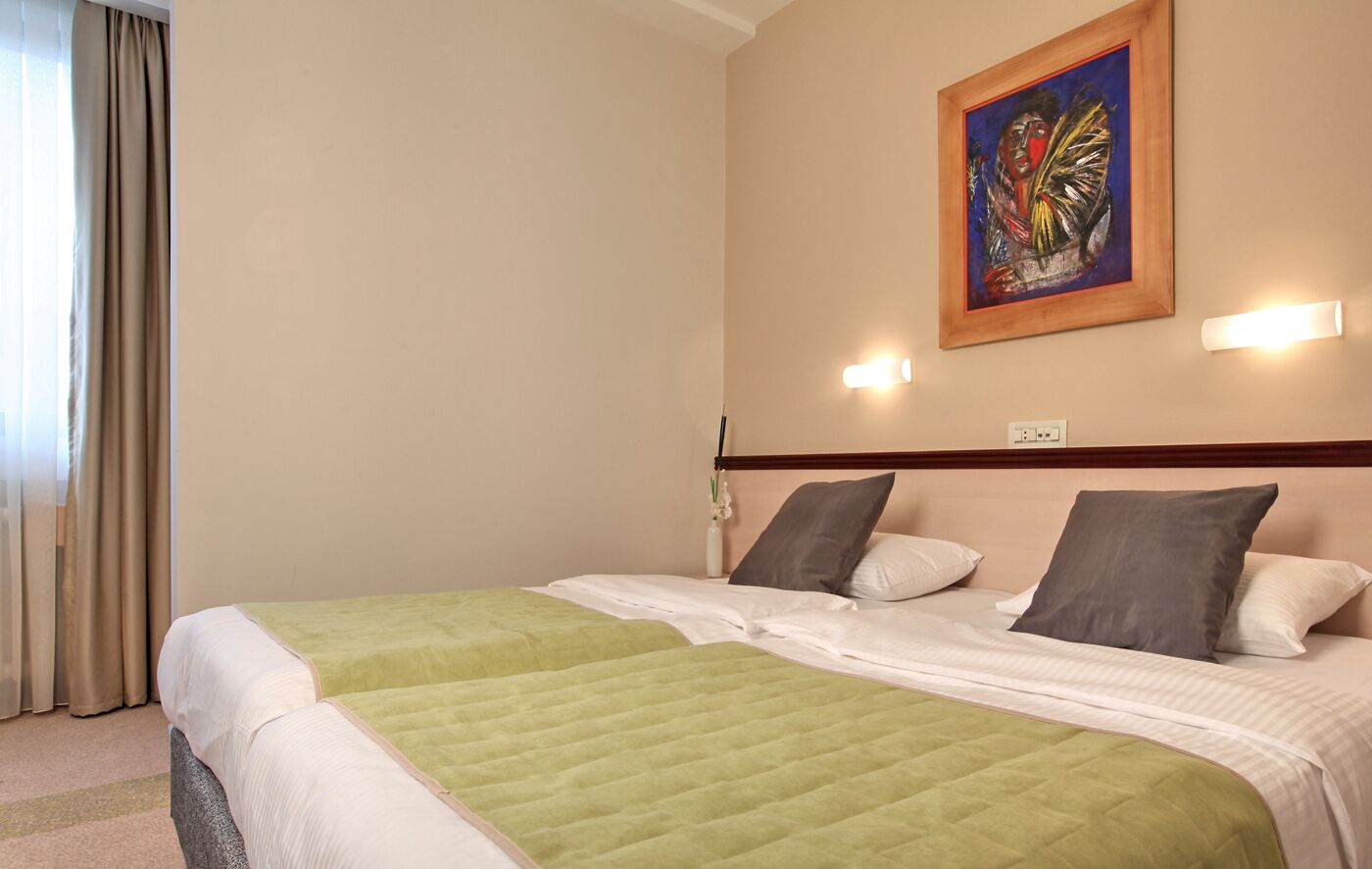 Una habitación de hotel con una cama, un cuadro en la pared y una ventana con cortinas.