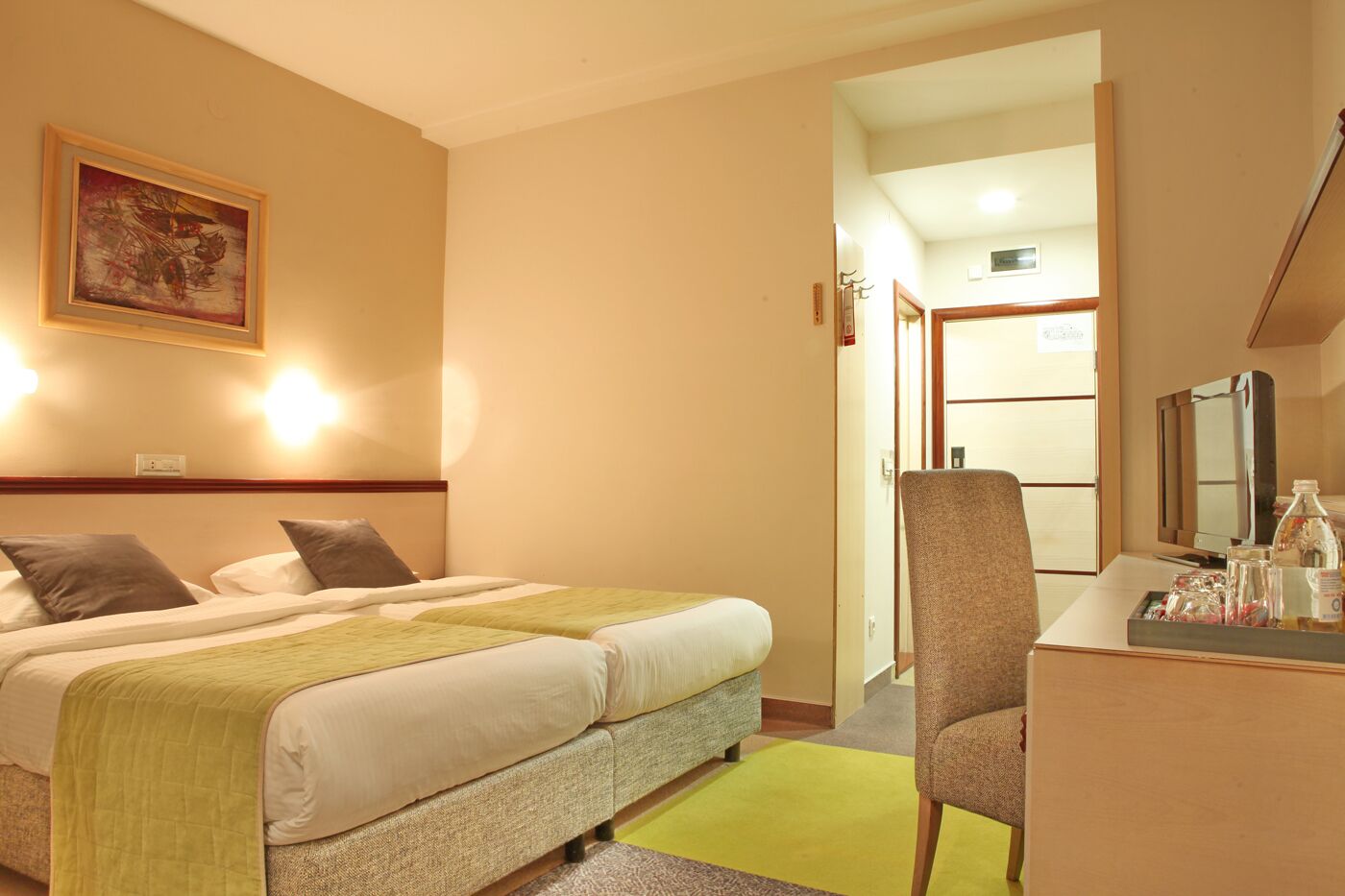 Una habitación de hotel con cama, escritorio, silla, televisor y un cuadro en la pared.