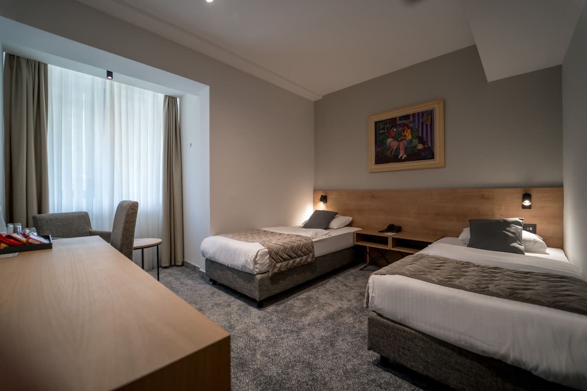A hotel room with two beds, a desk, a chair, and a painting on the wall.