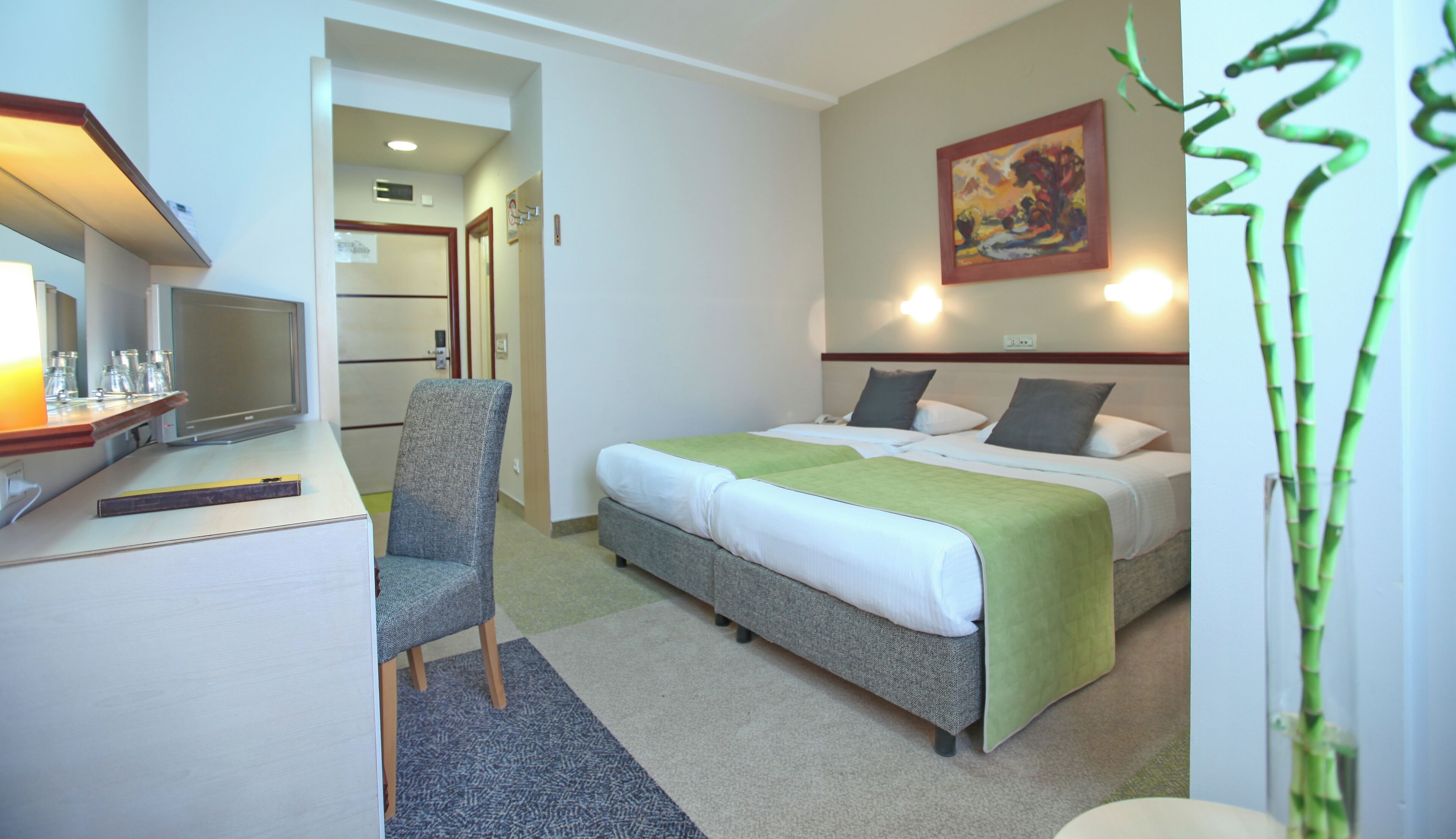 Habitación de hotel con cama, escritorio con computadora, silla y un cuadro en la pared.