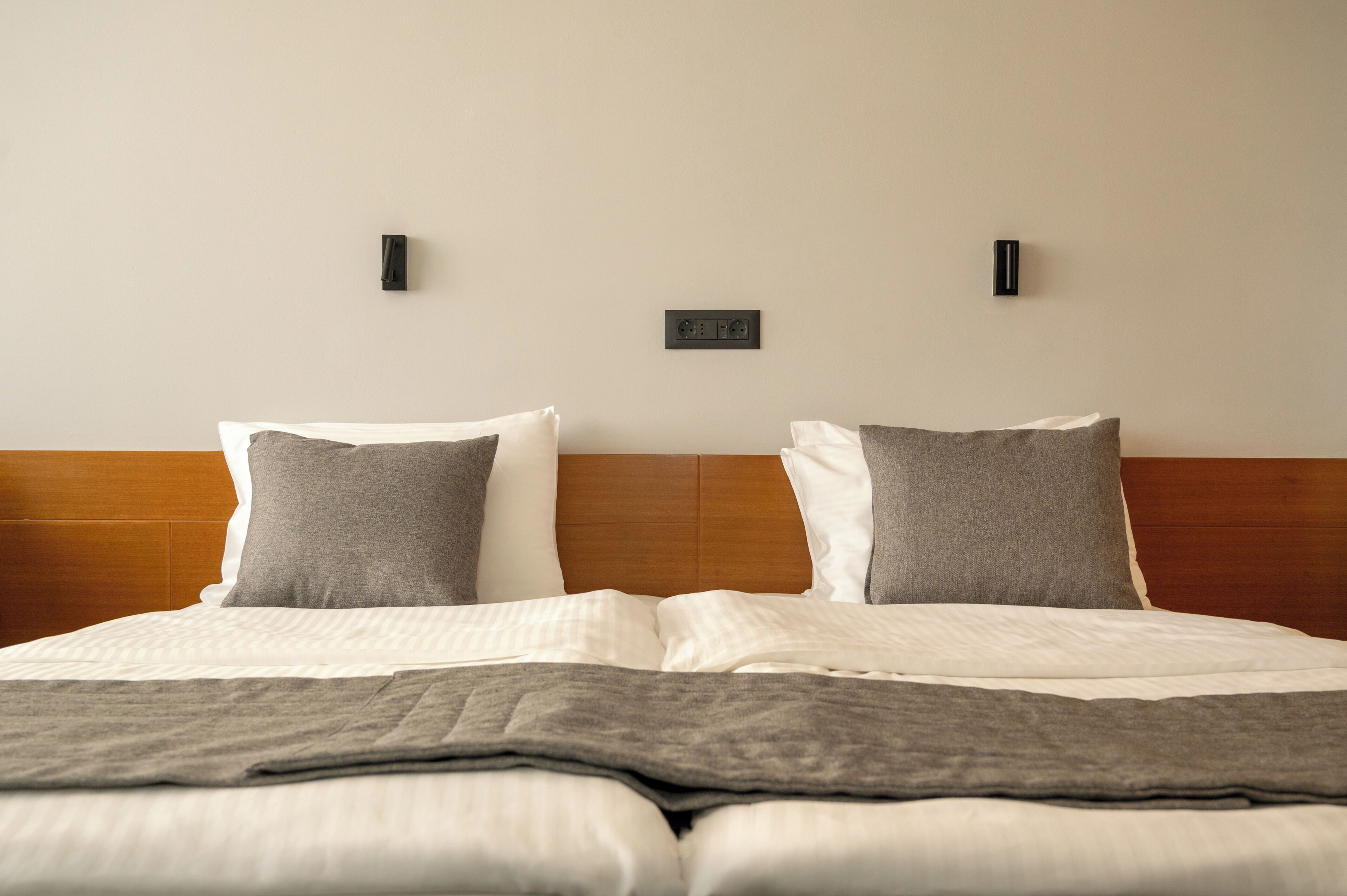 A neatly made bed with a wooden headboard, two bedside tables, and a wall socket.