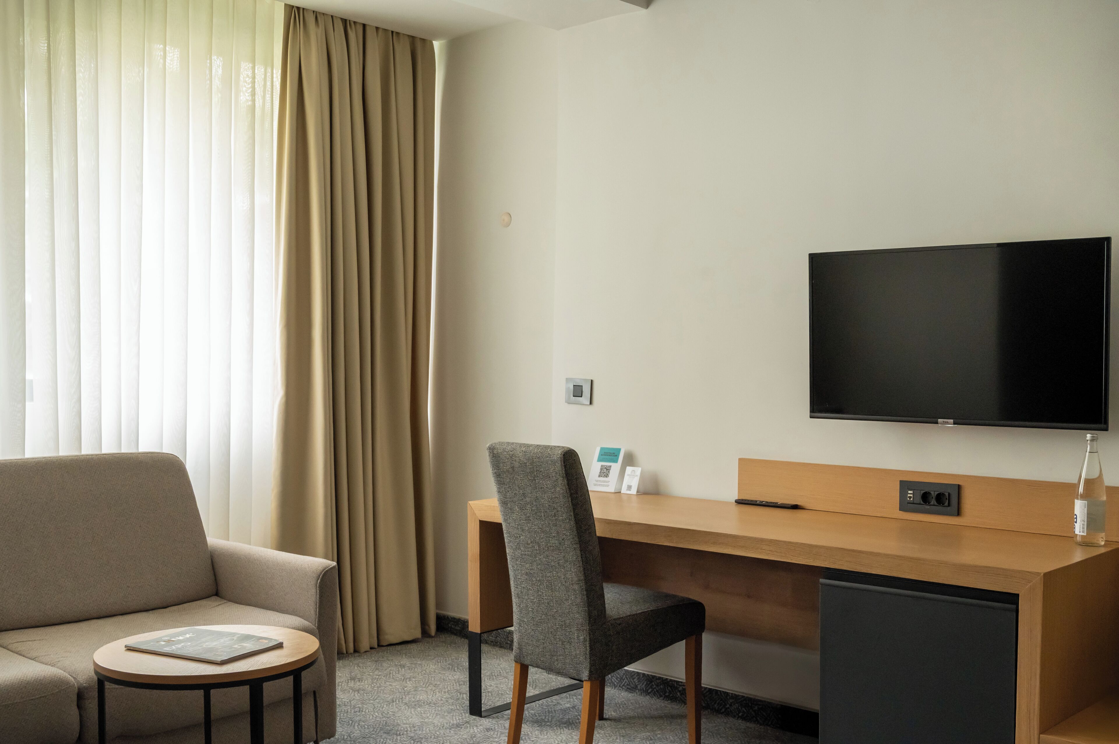 A hotel room with a sofa, a desk, a chair, a television, and a small table.