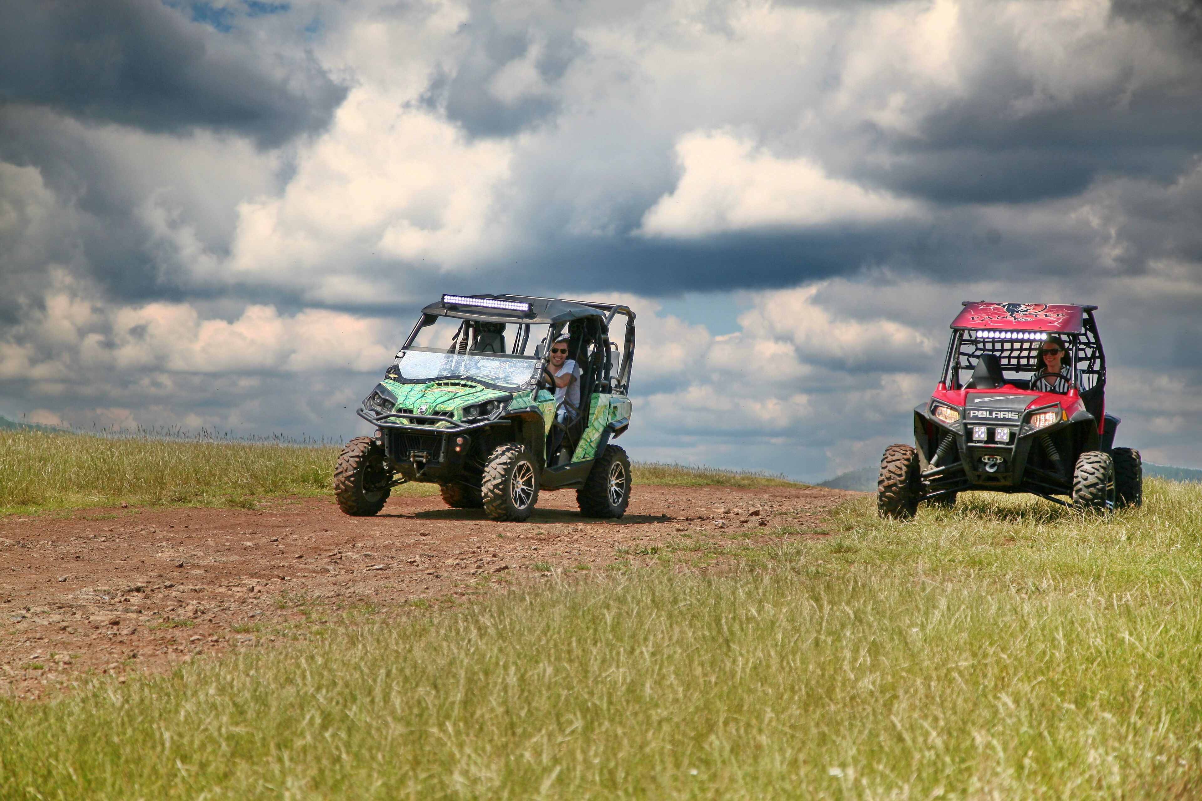Deux quads sur un chemin de terre dans un champ herbeux, sous un ciel nuageux.