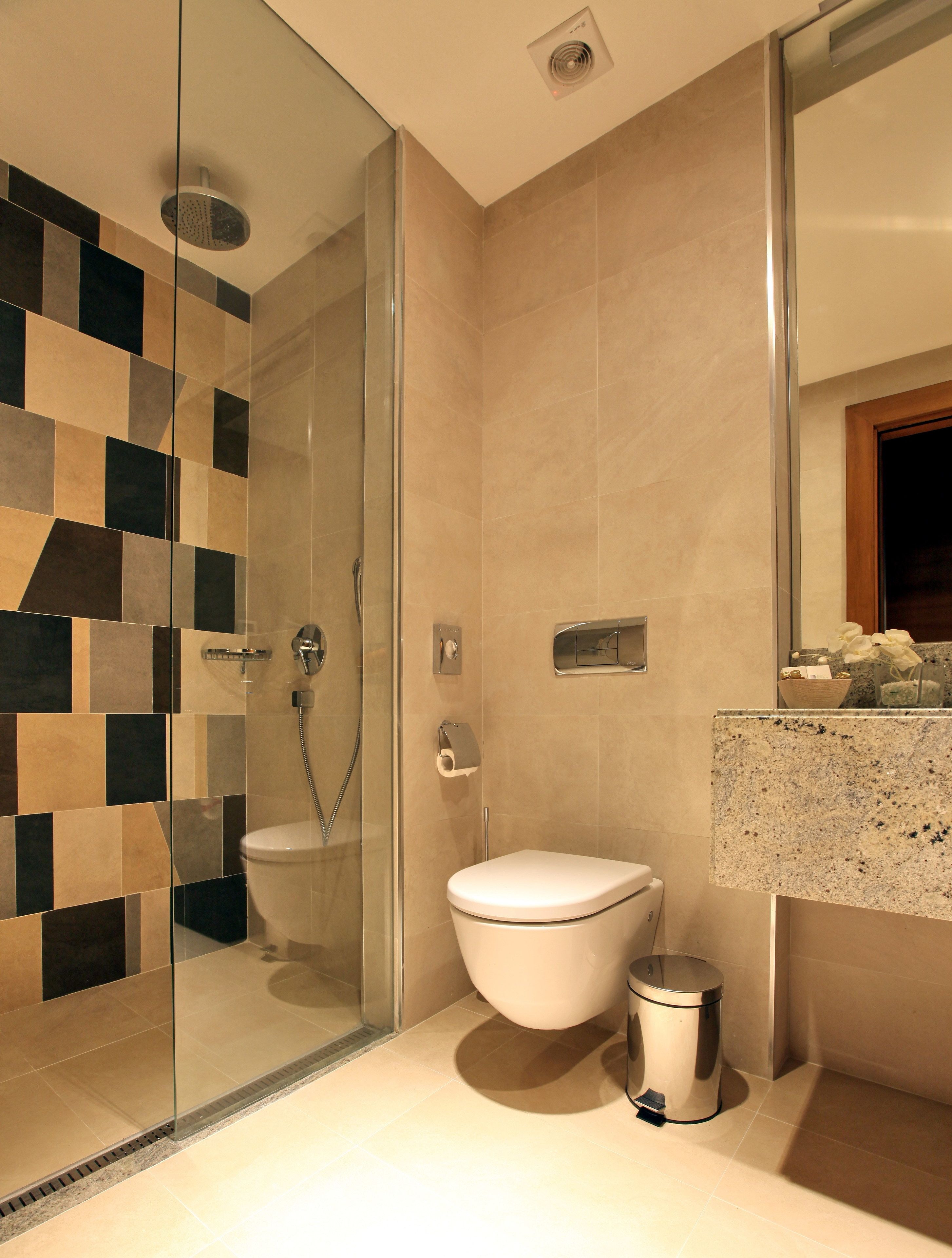 Un baño moderno con ducha de vidrio, inodoro y lavamanos con encimera de granito.