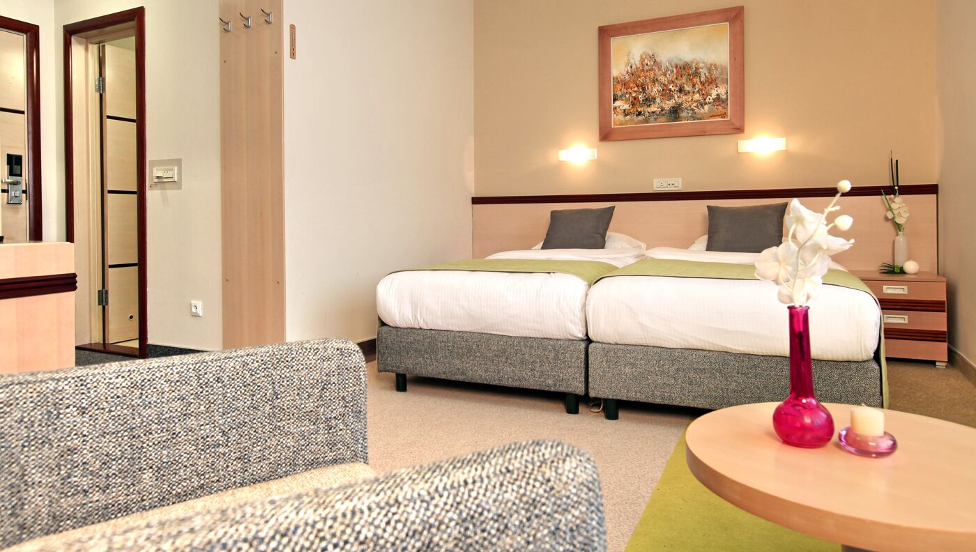 Una habitación de hotel con cama, una silla, una mesa con un florero y un cuadro en la pared.