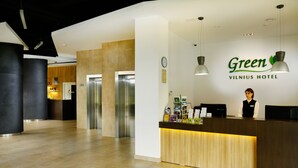 A hotel reception area with a wooden reception desk, a clock, and a sign for the Green Vilnius Hotel. - Green Vilnius Hotel (Vilnius)