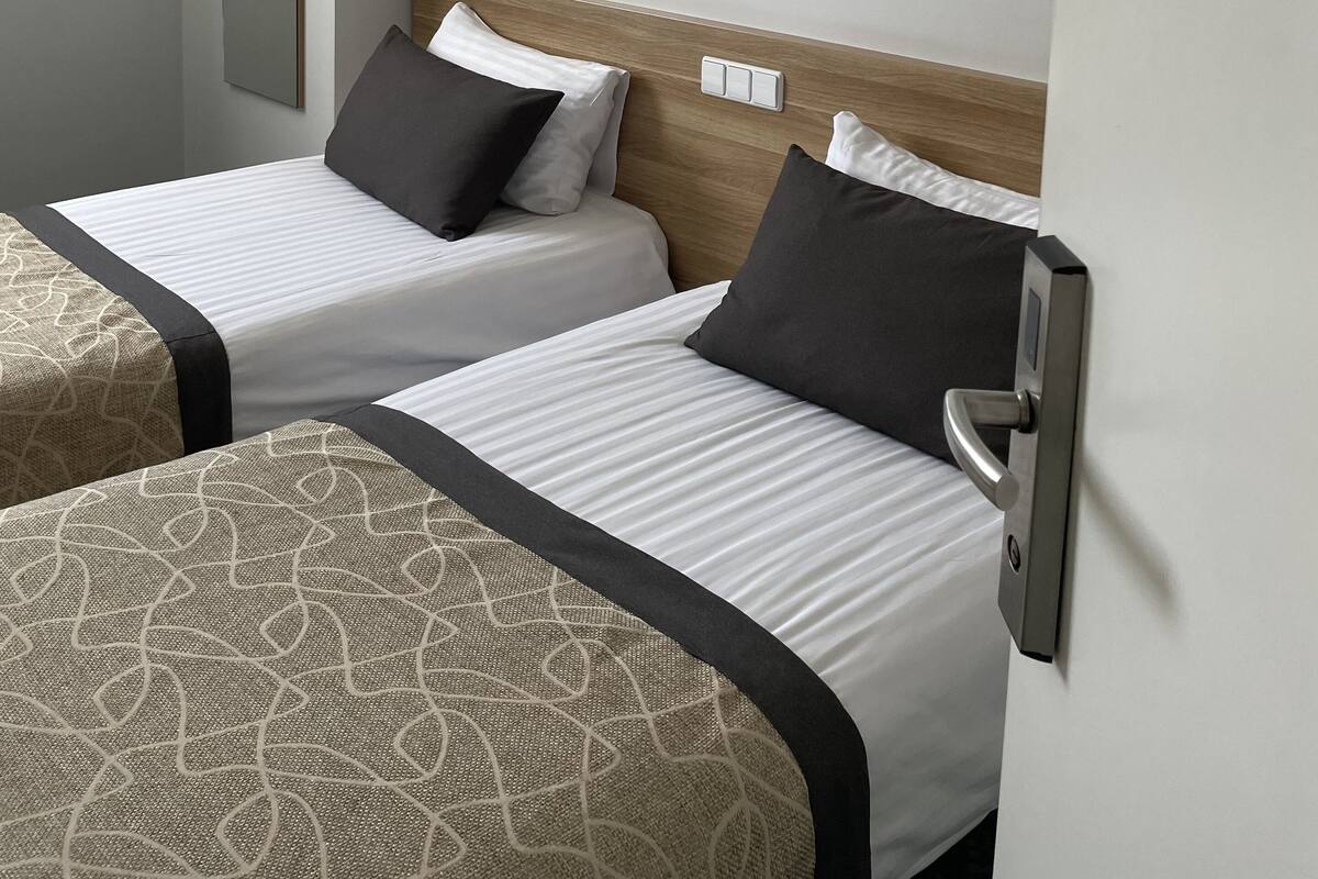 Habitación de hotel con dos camas, un espejo grande, un cuadro enmarcado en la pared y una puerta moderna.