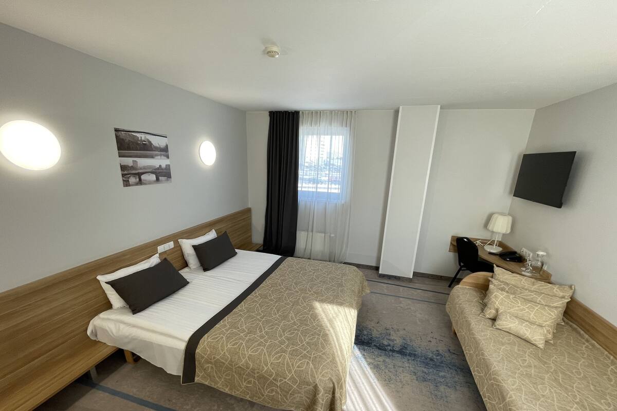 Habitación de hotel con una cama grande, un sofá, un escritorio con lámpara y un televisor en la pared.