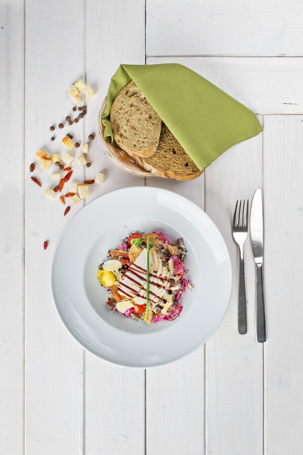 Une assiette blanche contenant une salade, une serviette verte et un pain sur une table en bois blanc.