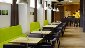 A restaurant interior with green booths, wooden tables, and hanging pendant lights. - Green Vilnius Hotel (Vilnius)