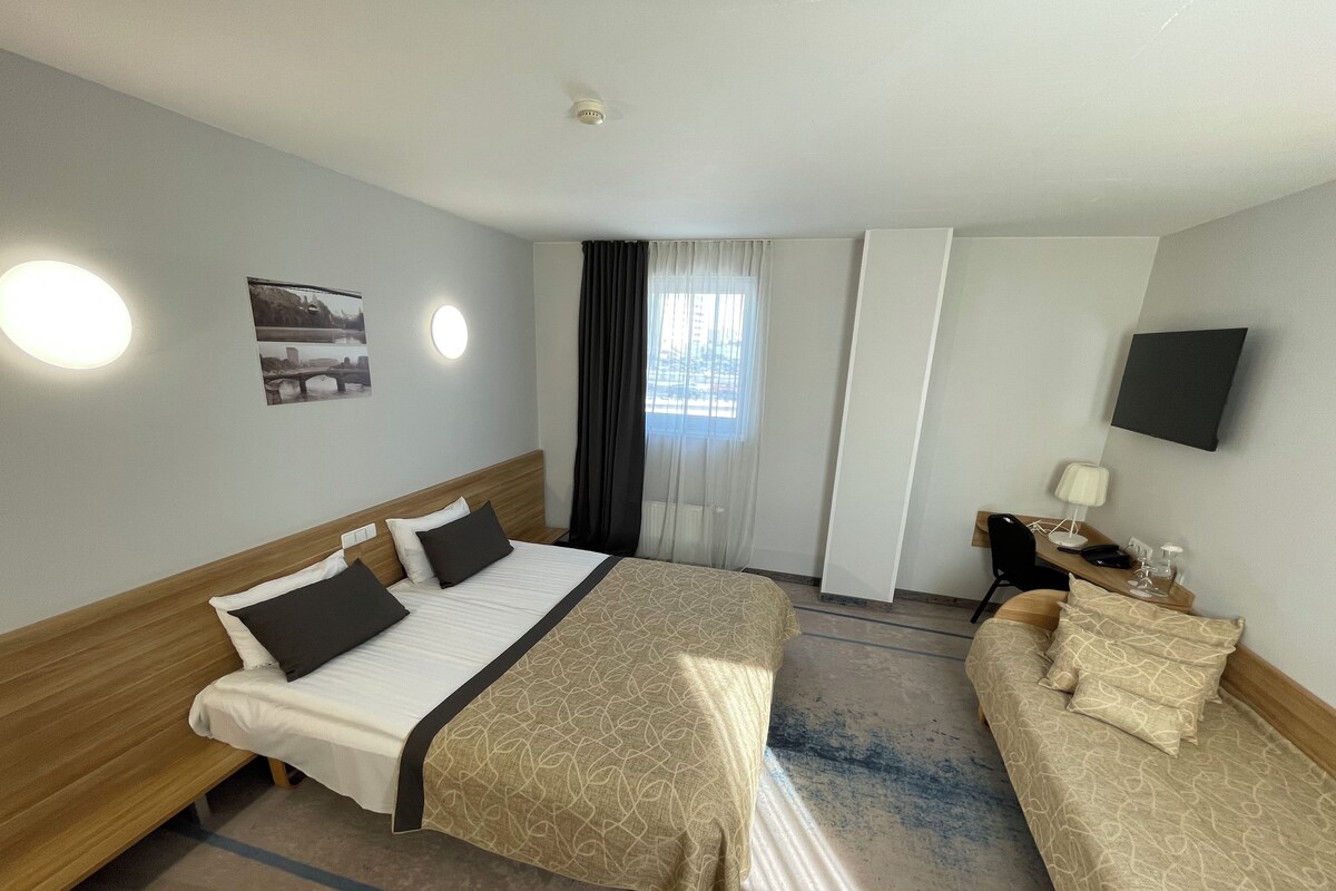 A hotel room with a large bed, a sofa, a desk with a lamp, and a TV on the wall.