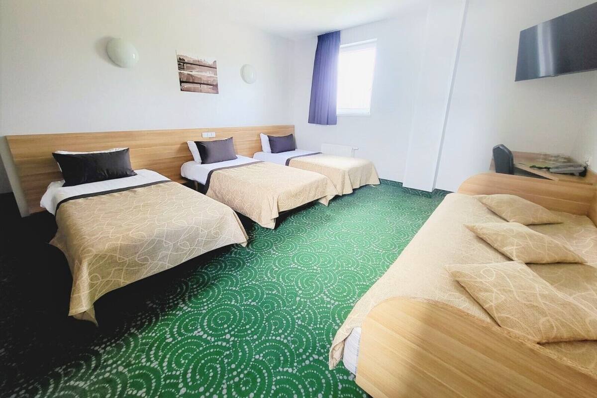 Habitación de hotel con dos camas individuales, un sofá, una ventana con cortinas y un televisor montado en la pared.