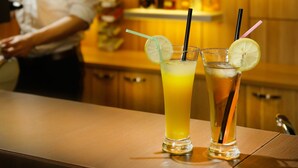 A bar with two drinks on the counter, a bartender in the background, and shelves with bottles. - Green Vilnius Hotel (Vilnius)