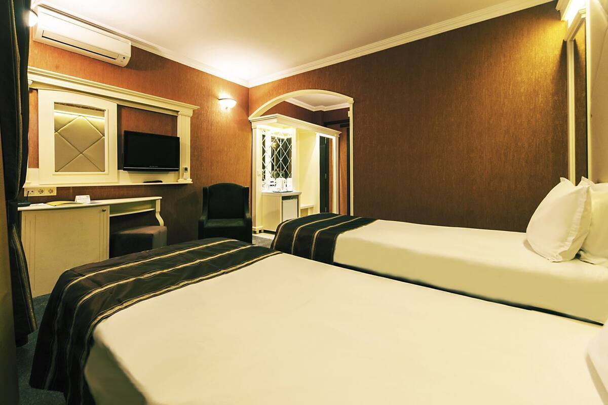 Habitación de hotel con cama, escritorio, silla, televisión y baño visible a través de un arco.