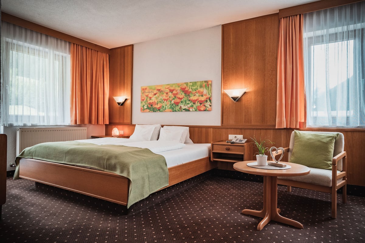 Une chambre d’hôtel avec un lit, une chaise, une petite table avec une plante et un tableau au mur.
