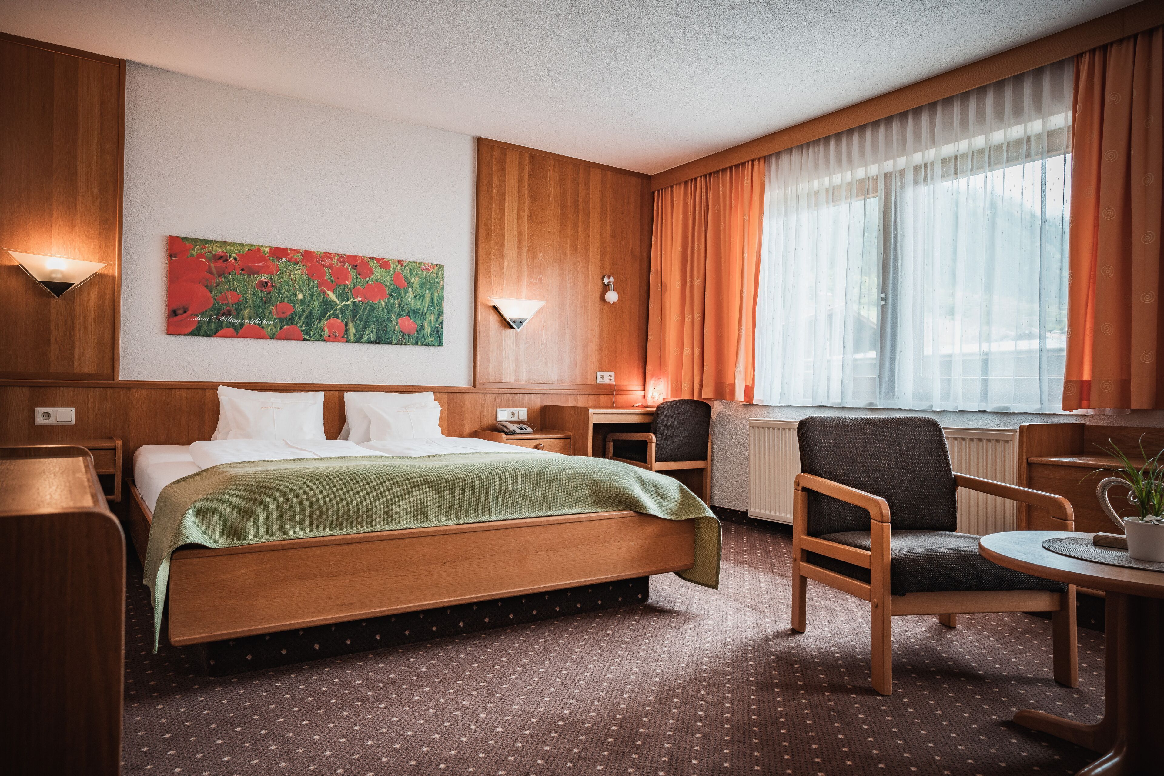 Hotelkamer met een houten bed, een bureau, een stoel en een raam met gordijnen.