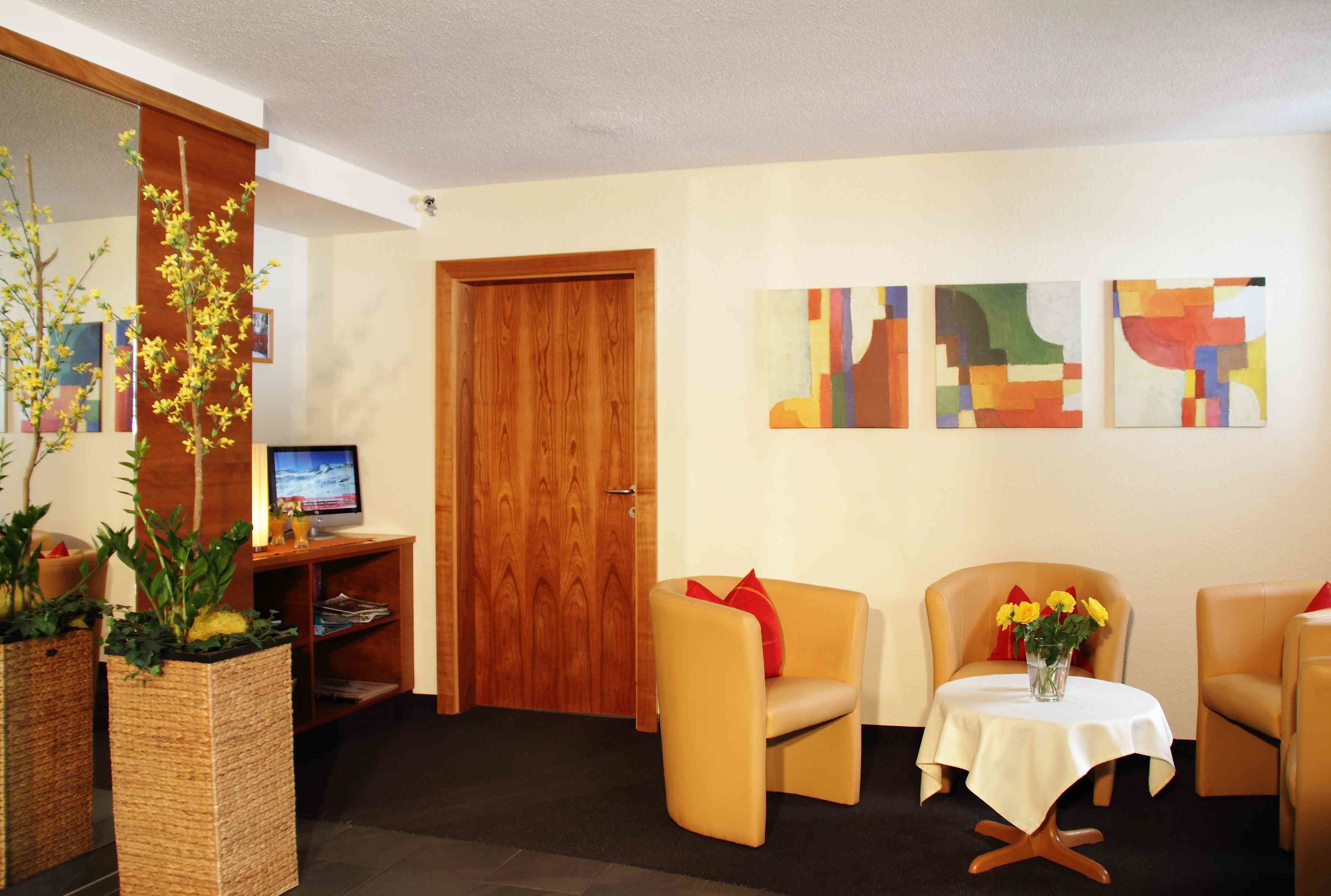 Una habitación moderna con puerta de madera, televisor, dos sillones, una mesita con un jarr ón de flores y arte abstracto en la pared.