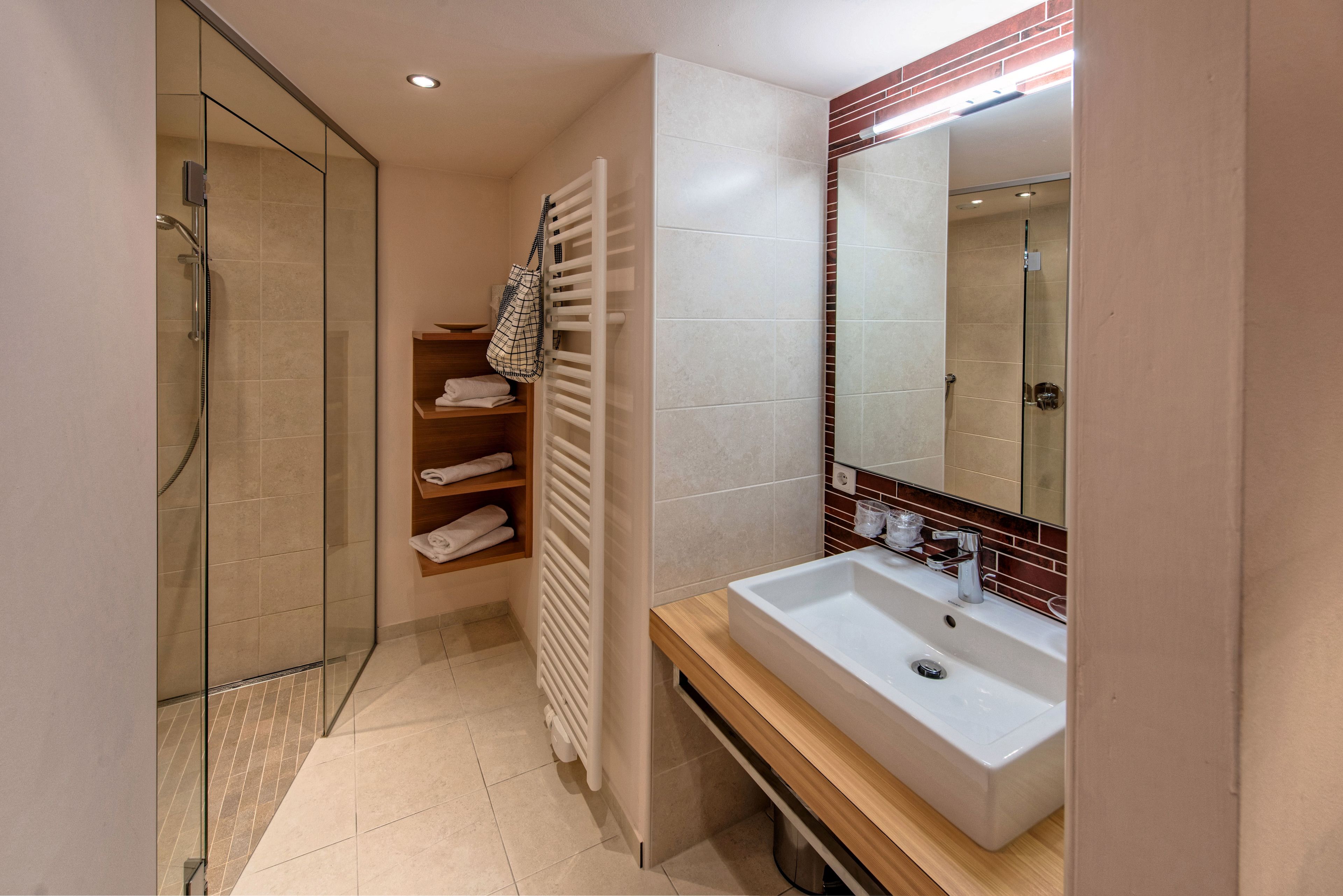 Un baño moderno con ducha envuelta en vidrio, un lavabo blanco y un perchero para toallas.