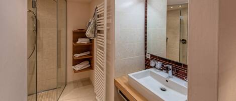 Un baño moderno con ducha envuelta en vidrio, un lavabo blanco y un perchero para toallas.