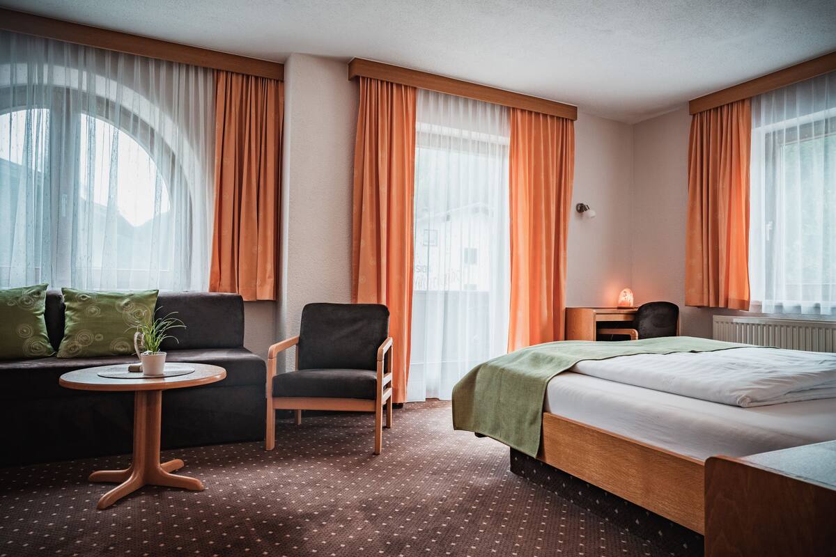 Une chambre d’hôtel avec un lit, un canapé, une chaise, une petite table et une plante en pot.