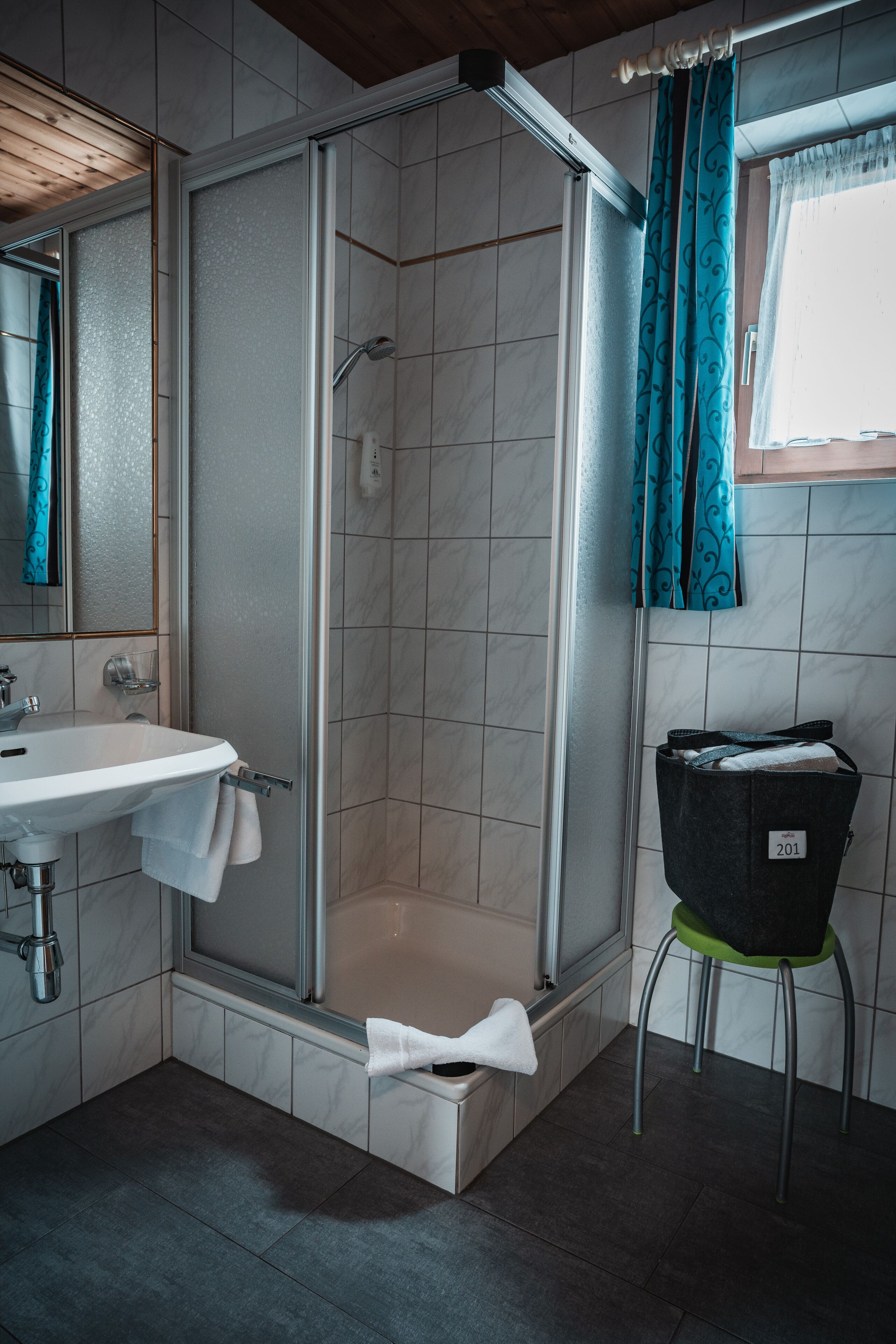 A bathroom with a glass-enclosed shower, a sink, and a green stool.