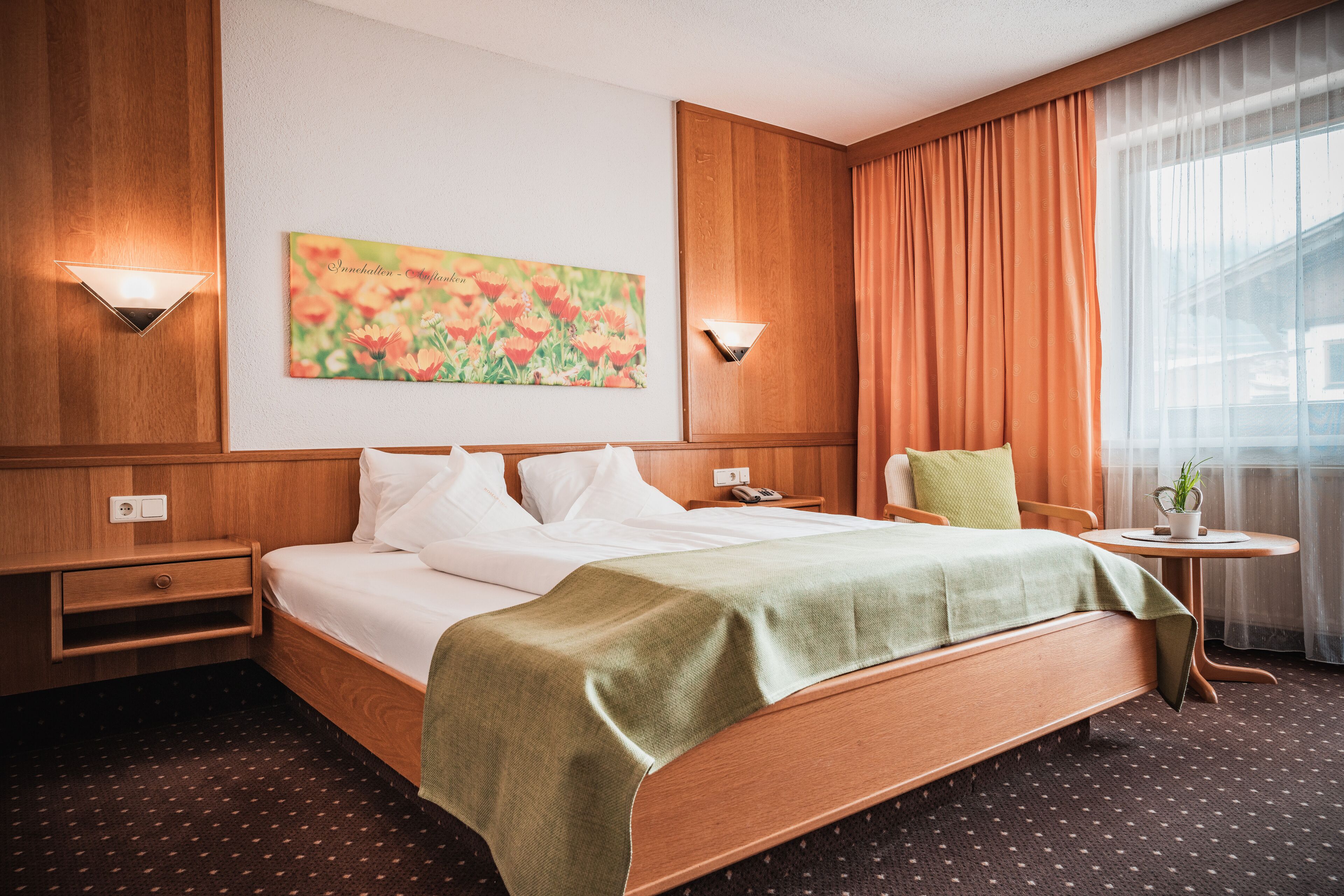 Habitación de hotel con una cama grande, una mesita con una planta, una silla y un cuadro en la pared.