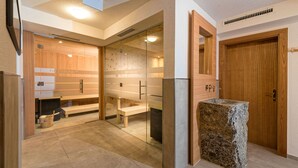 Una sala de sauna con bancos de madera, puertas de vidrio, un banco de piedra y una puerta de madera.