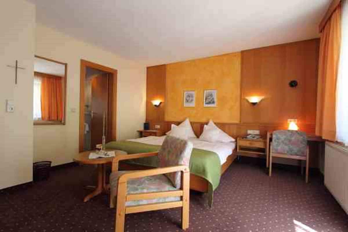 Une chambre d’hôtel comprenant un lit, deux tables de chevet, une chaise, une petite table et une fenêtre avec des rideaux.
