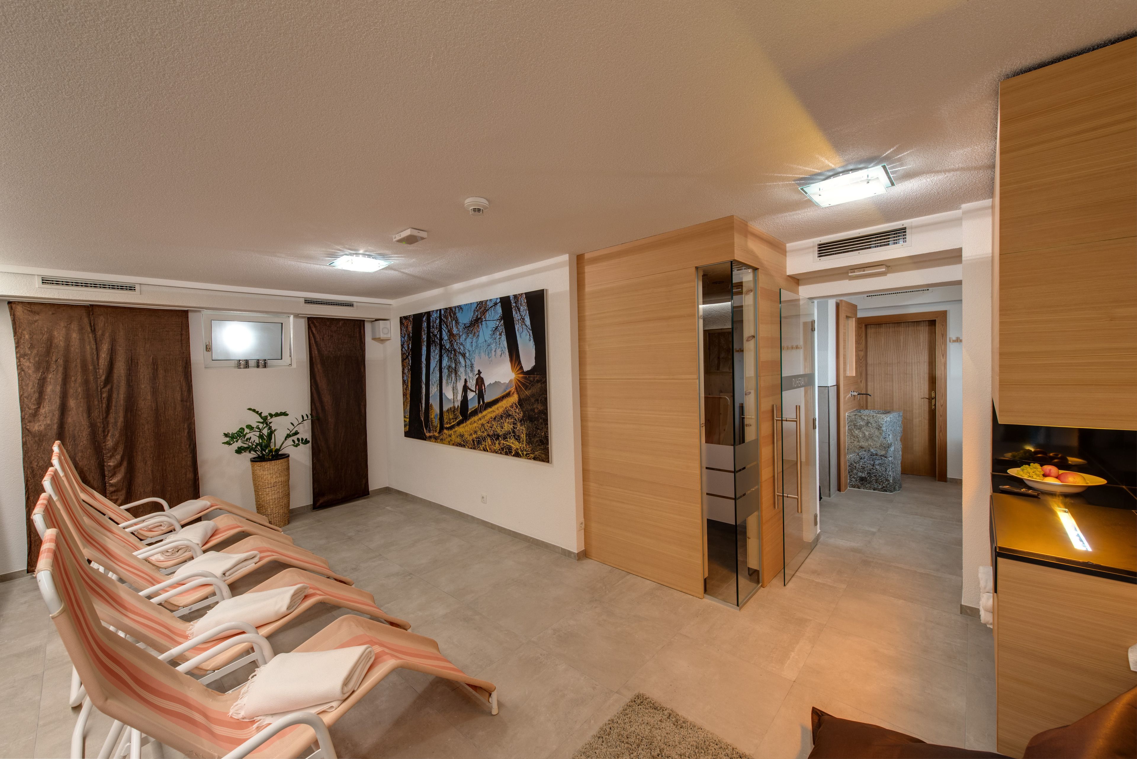 A modern hotel room with a seating area, a painting, a kitchen, and a bathroom.