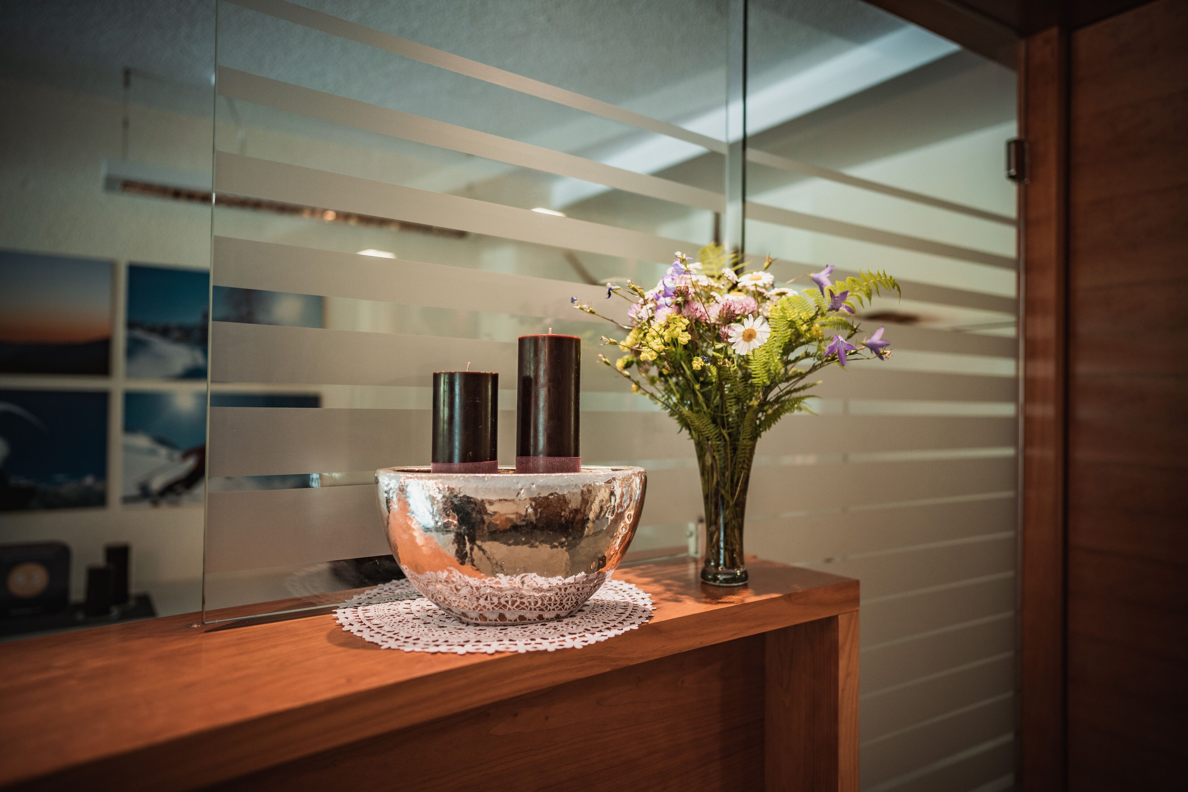 A wooden reception desk with a decorative bowl, two candles, and a vase of flowers.