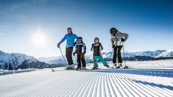 A family on a snowy ski slope with mountains in the background.