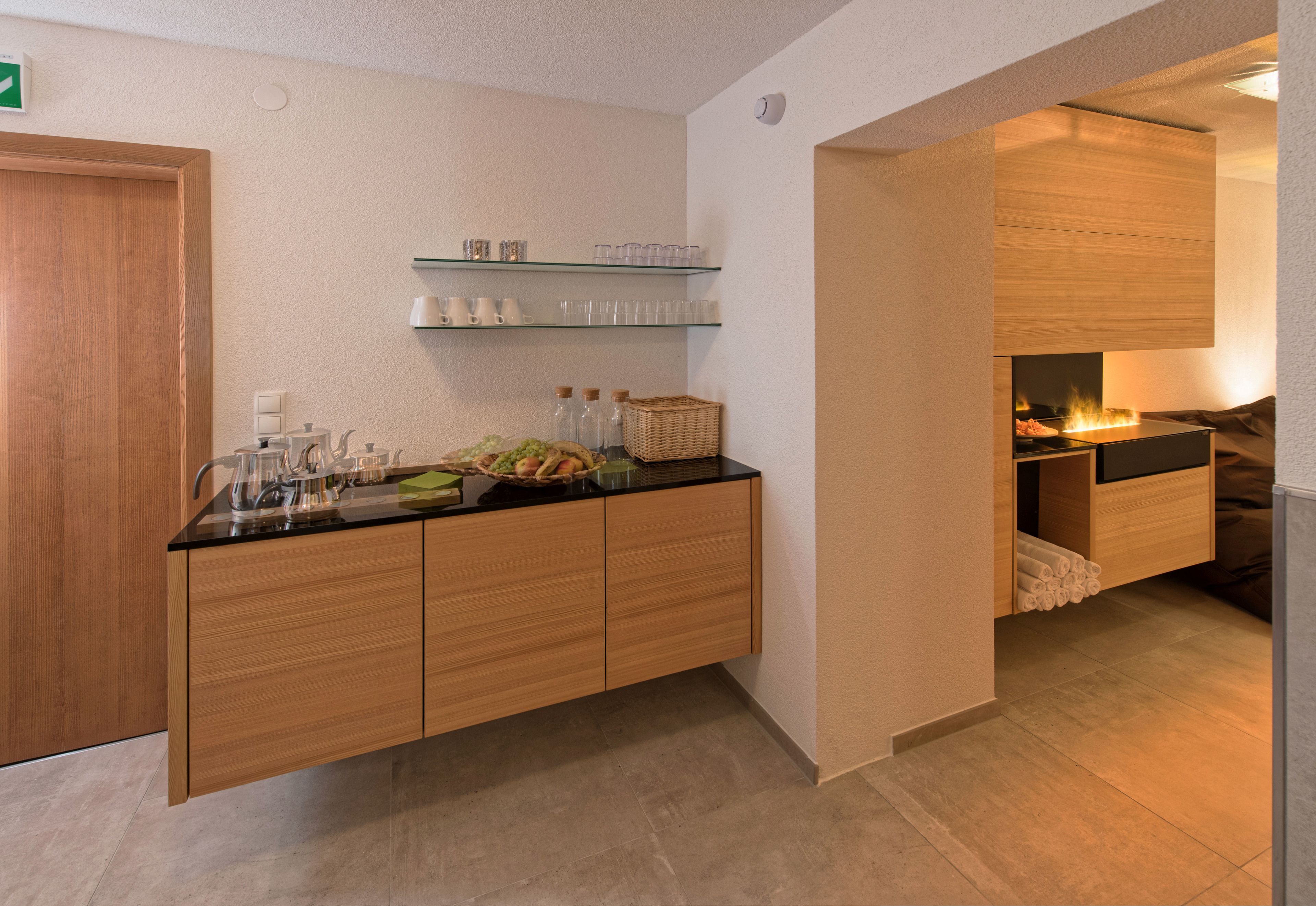 A modern kitchen with wooden cabinets, a black countertop, and glass shelves above.