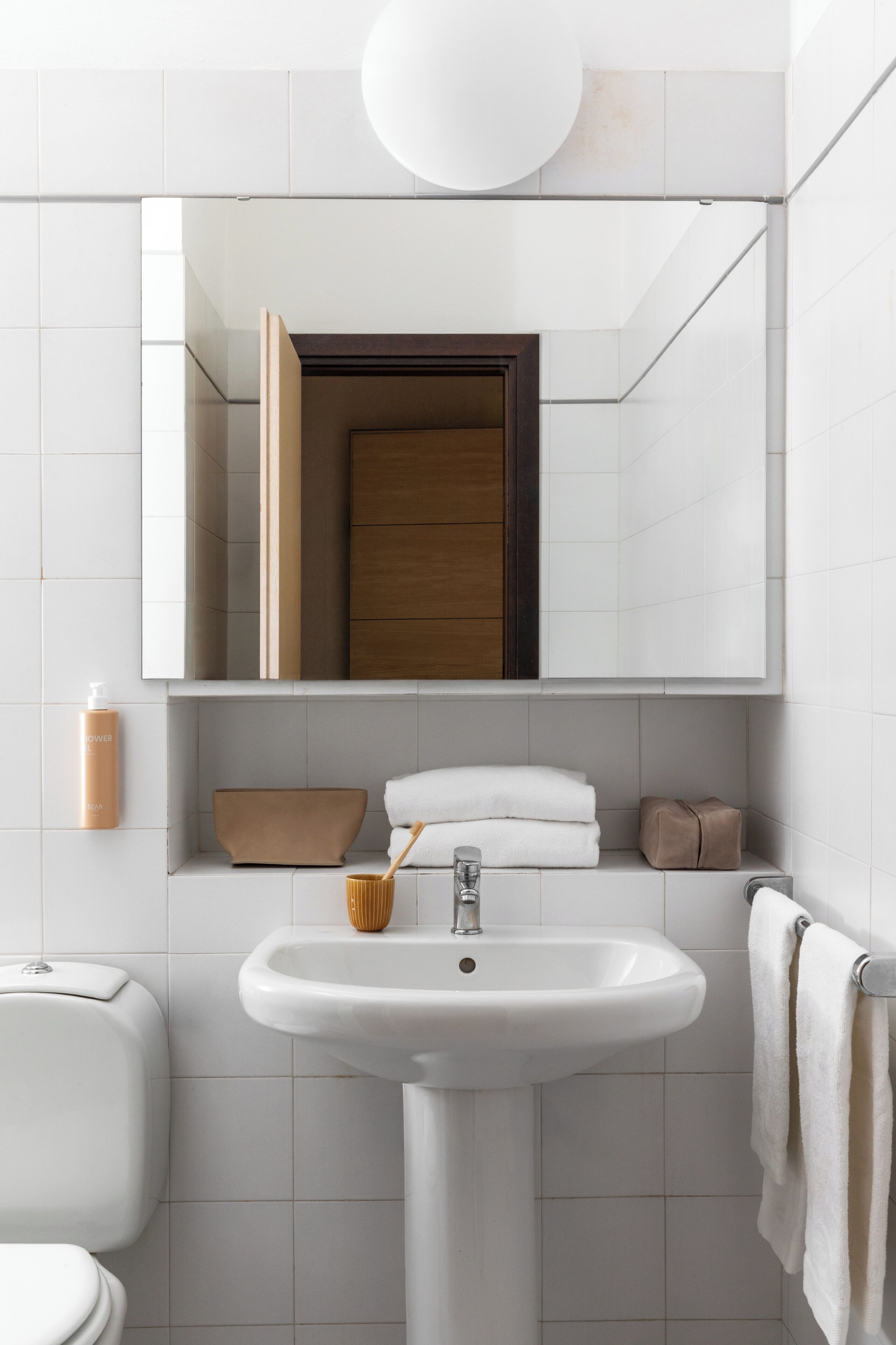 Une salle de bain avec un lavabo blanc, un miroir, une porte en bois et un porte-serviettes.