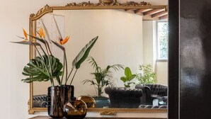 A wooden cabinet with a mirror above it, reflecting a plant and a window. - Hotel Al Sant andrea (Sarzana)