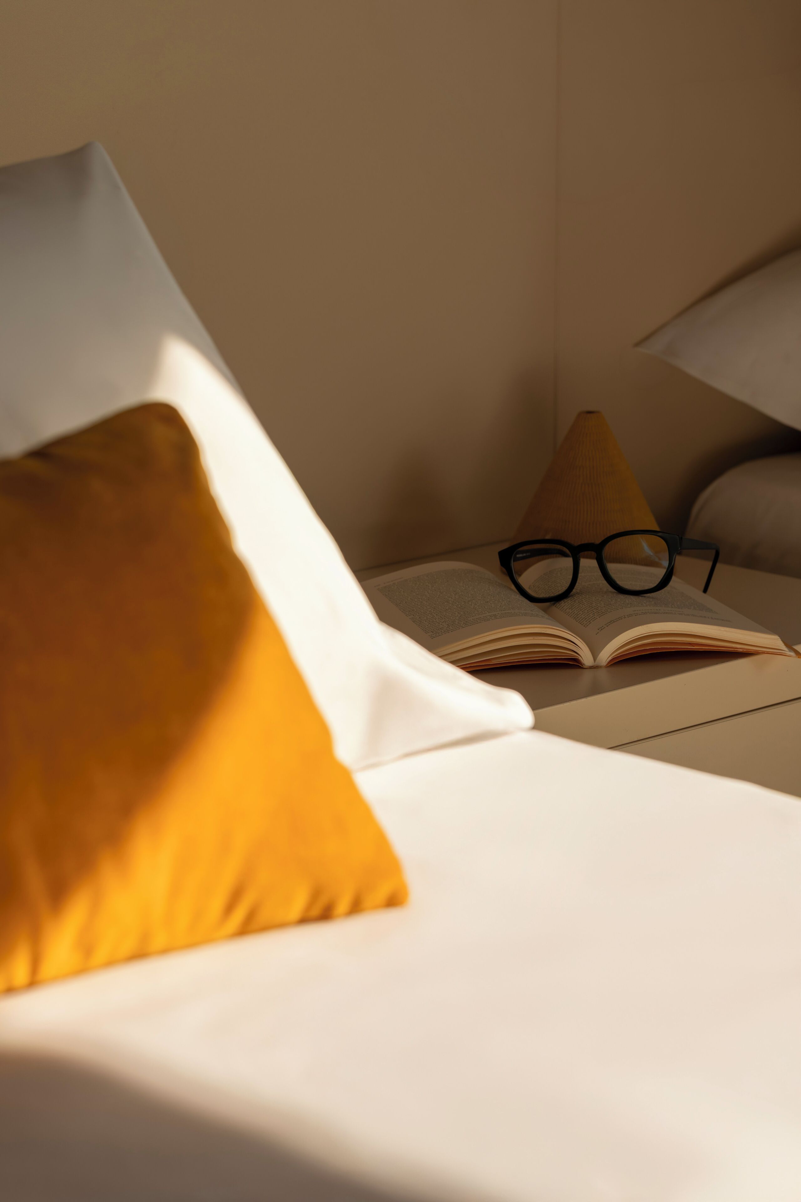 Ein Bett mit einem weißen Kopfkissen und einem offenen Buch, auf dem eine Brille liegt.