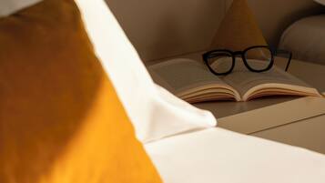 Ein Bett mit einem weißen Kopfkissen und einem offenen Buch, auf dem eine Brille liegt.