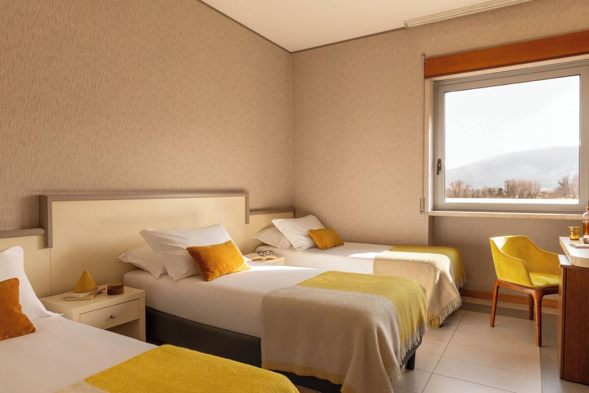 Une chambre d’hôtel avec deux lits, un bureau, une chaise et une grande fenêtre.