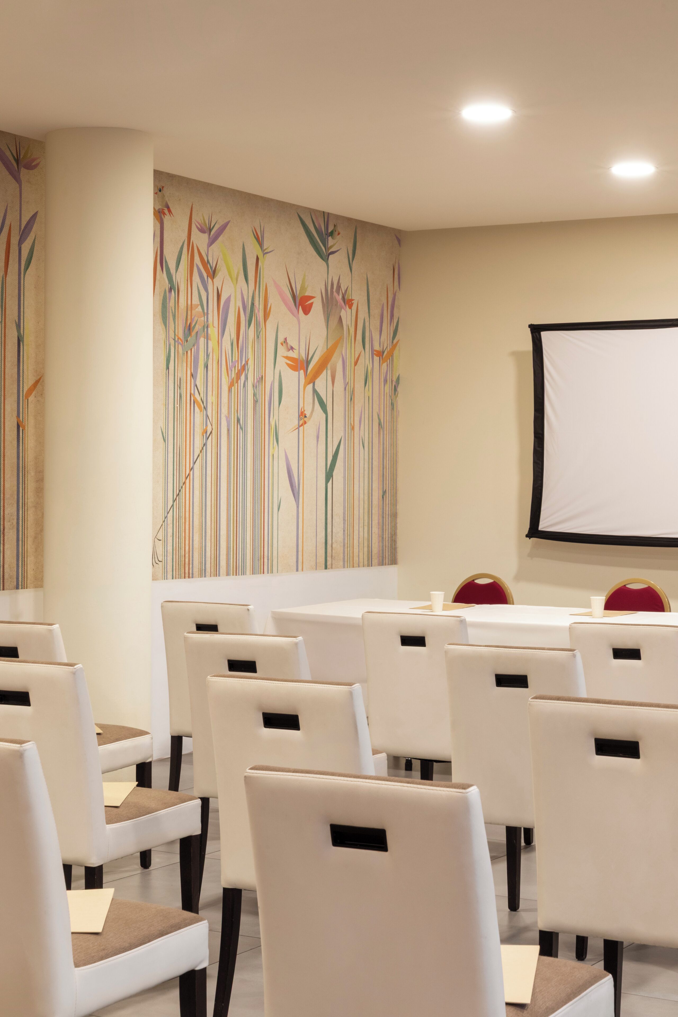 Ein Konferenzraum mit weißen Stühlen, einer Projektorleinwand und farbenfroher abstrakter Wandkunst.
