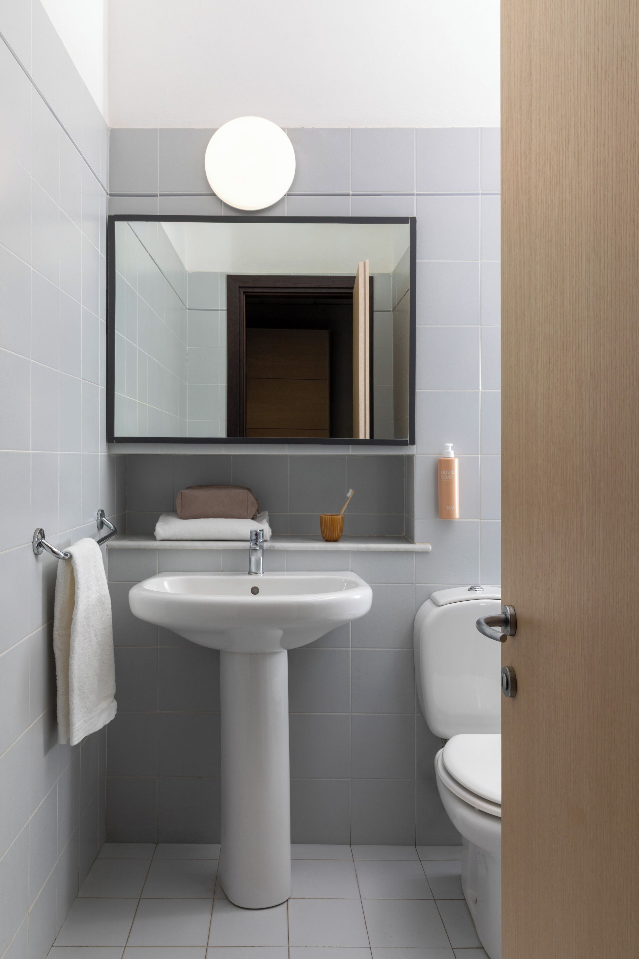 A bathroom with a pedestal sink, a toilet, a mirror above the sink, and a towel rack.