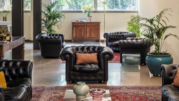 A spacious living area with leather sofas, a coffee table, and a large window providing a view of greenery outside. - Hotel Al Sant andrea (Sarzana)