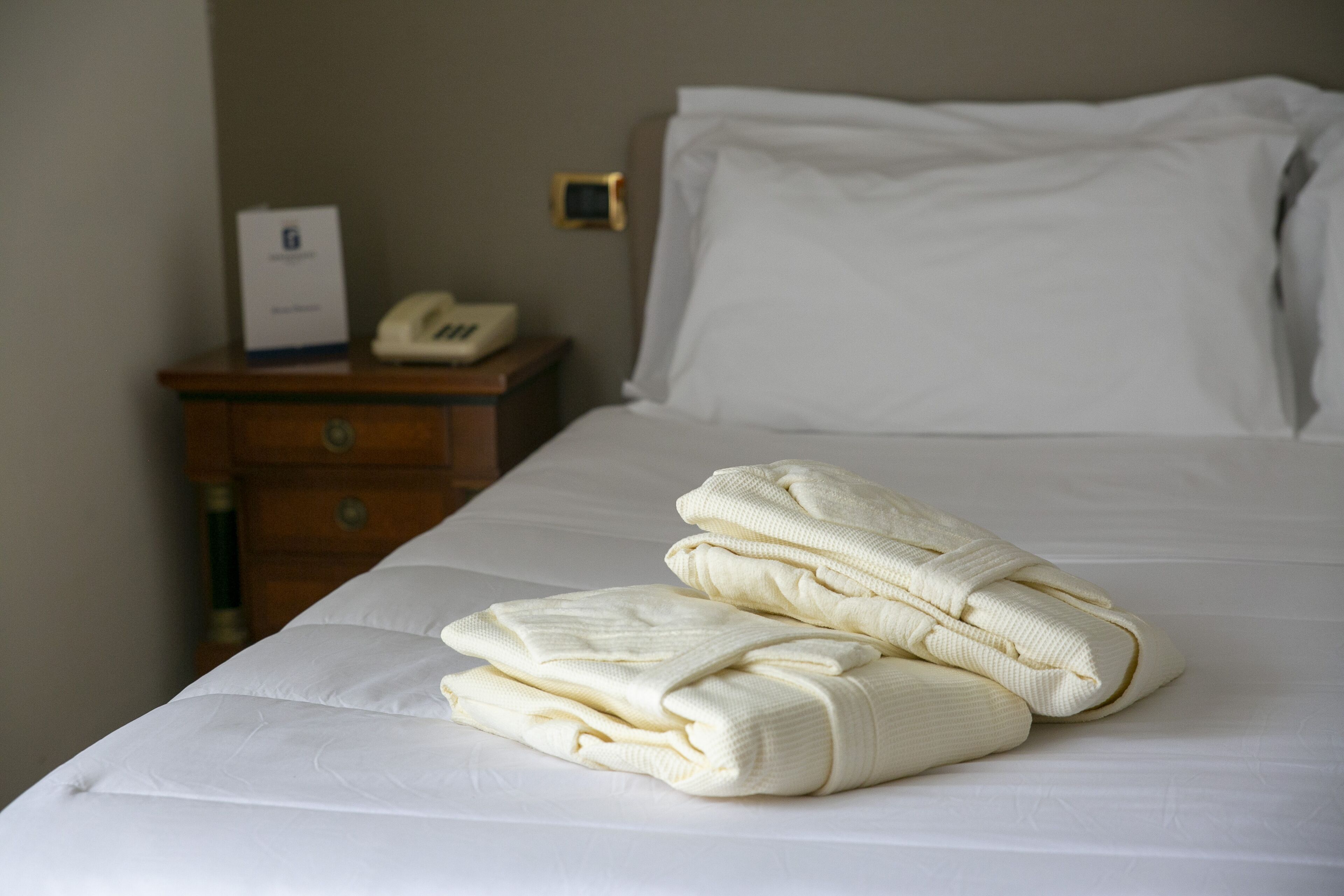A neatly made bed with folded towels and a bedside telephone on a wooden nightstand.
