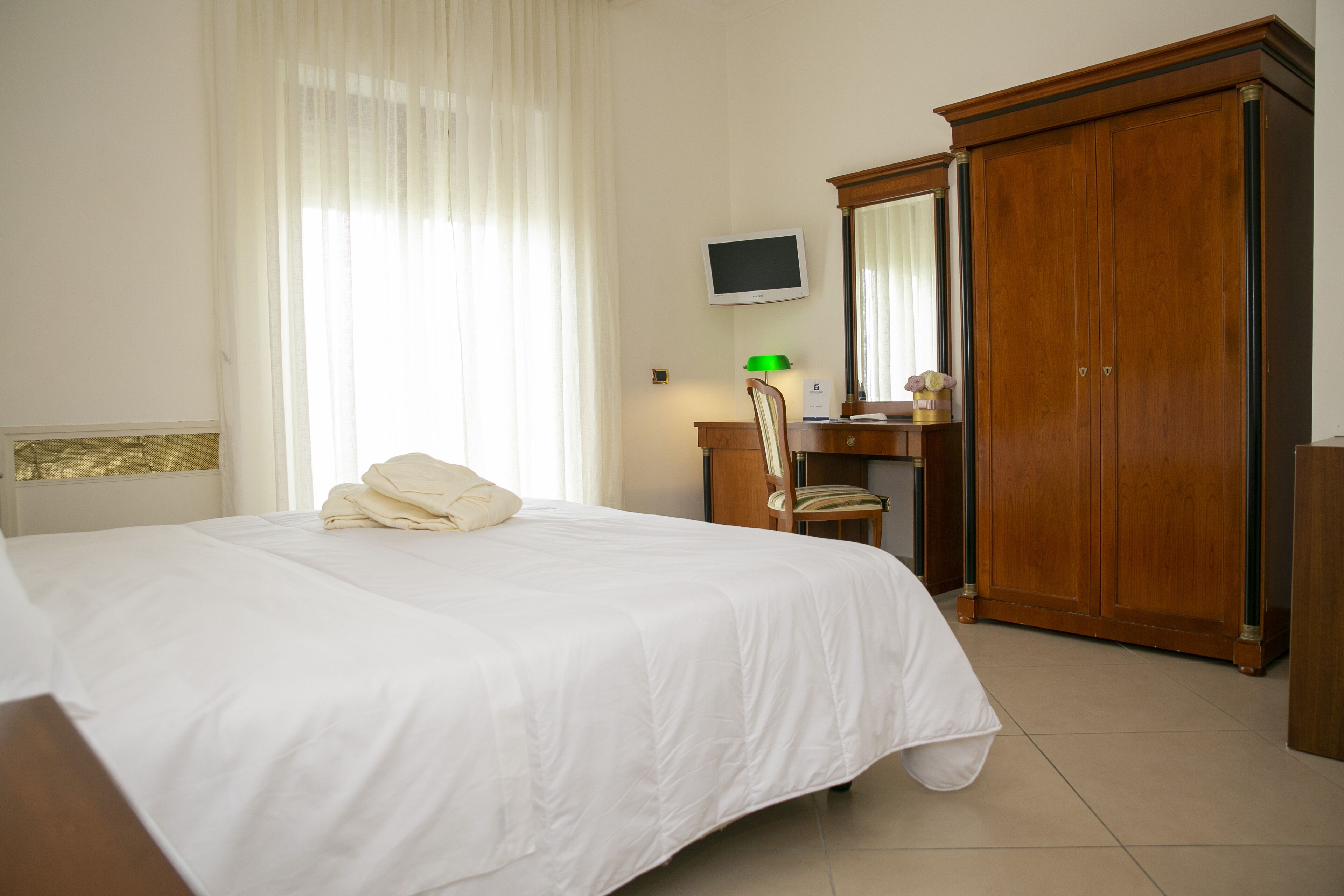 Una habitación de hotel con cama, escritorio, silla, televisor y armario.