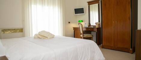Una habitación de hotel con cama, escritorio, silla, televisor y armario.