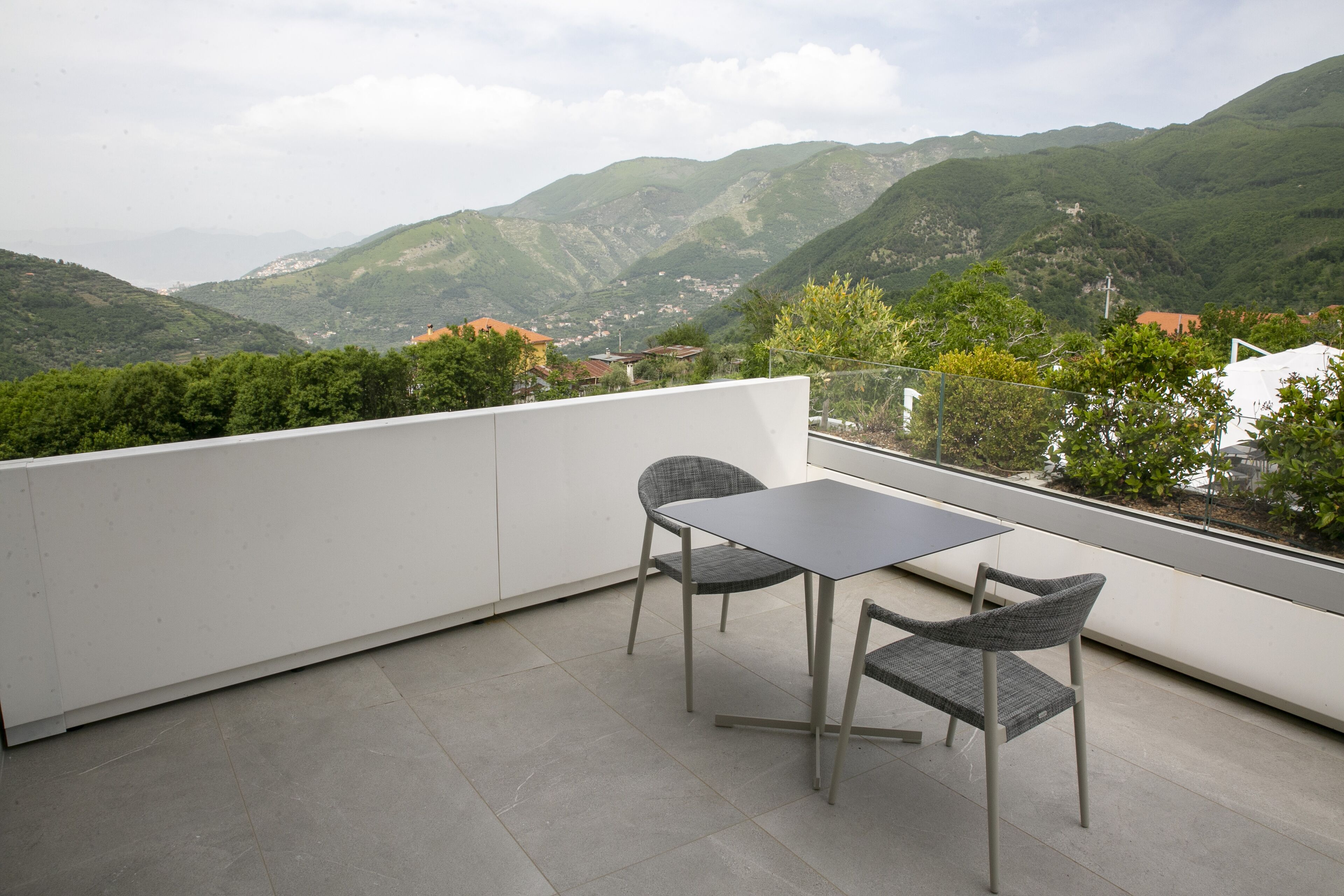 Un balcone con un tavolo e due sedie, affacciato su un paesaggio montuoso.