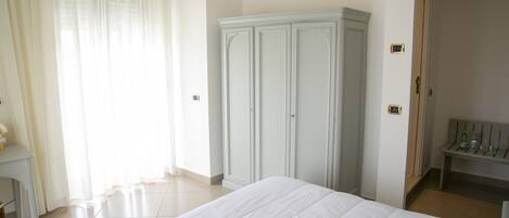 Habitación de hotel con una cama grande, un armario, un banco con artículos de aseo y una puerta que da a otra habitación.