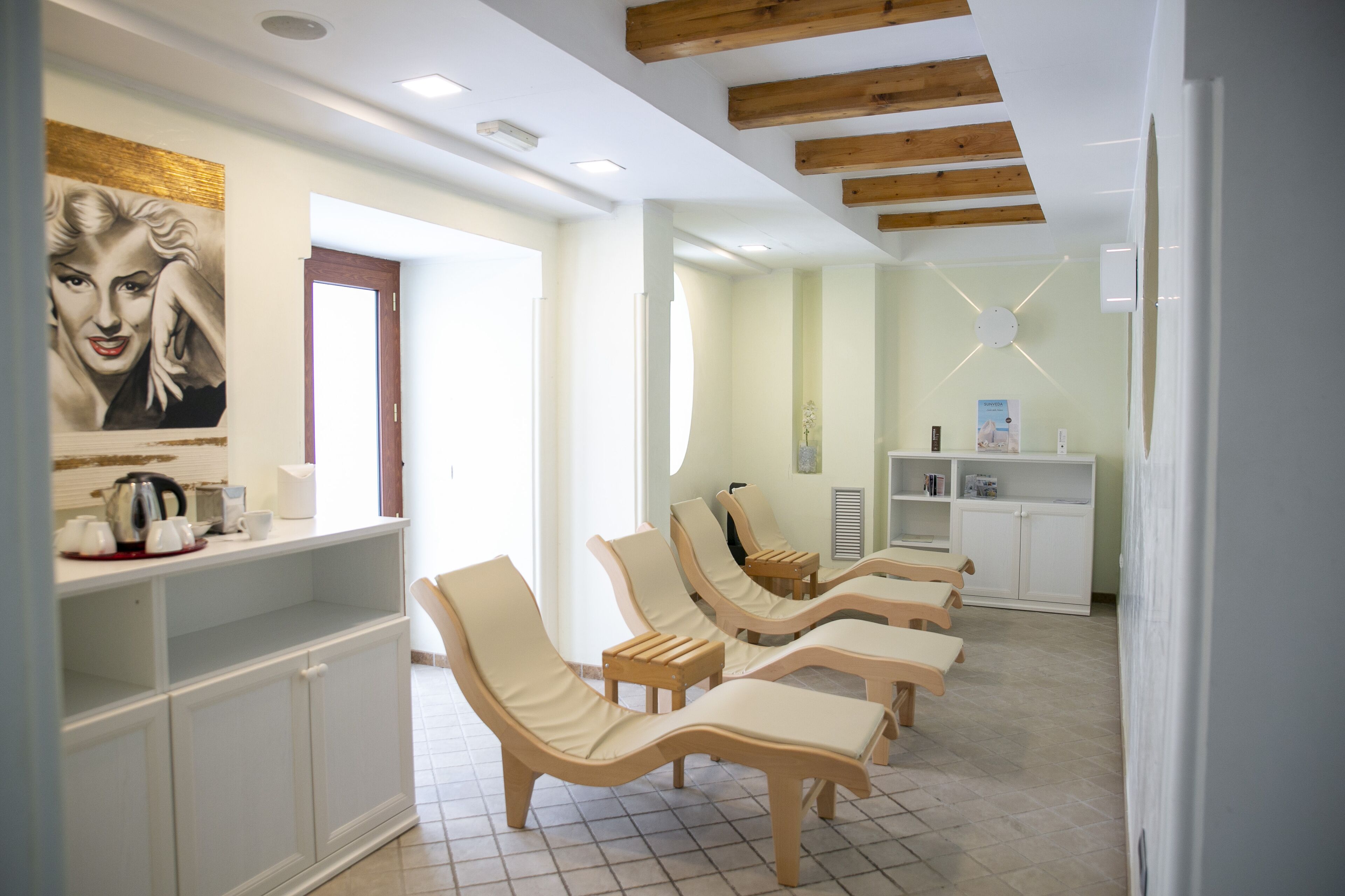 A room with reclining chairs, a coffee station, and a reception area with a painting.