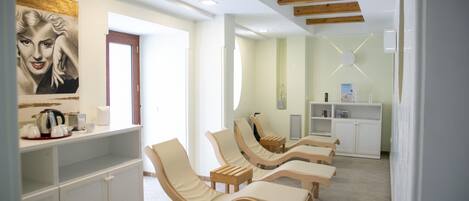 A room with reclining chairs, a coffee station, and a reception area with a painting.