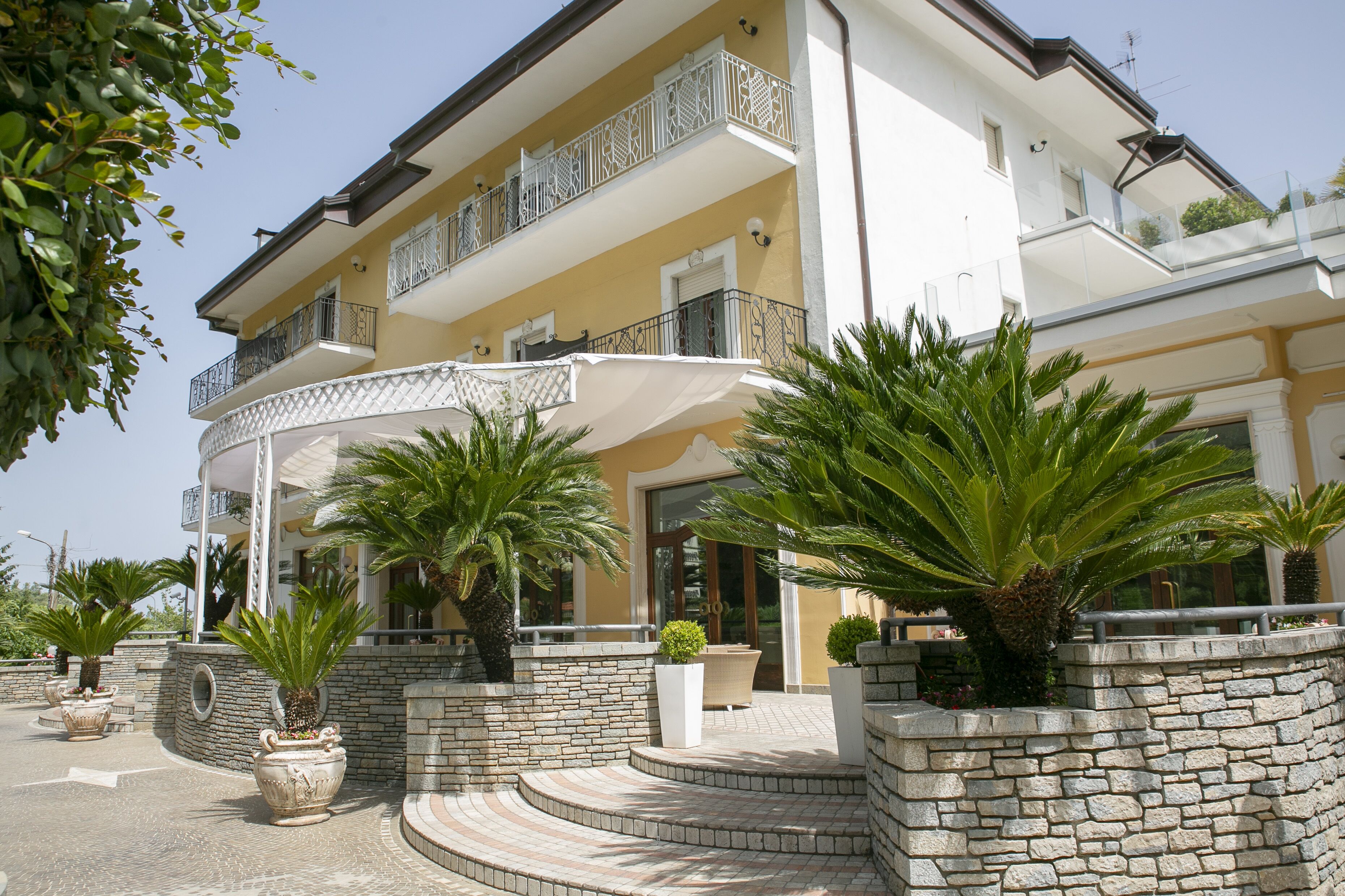 A multi-story building with a stone facade, balconies with white railings, and potted plants.