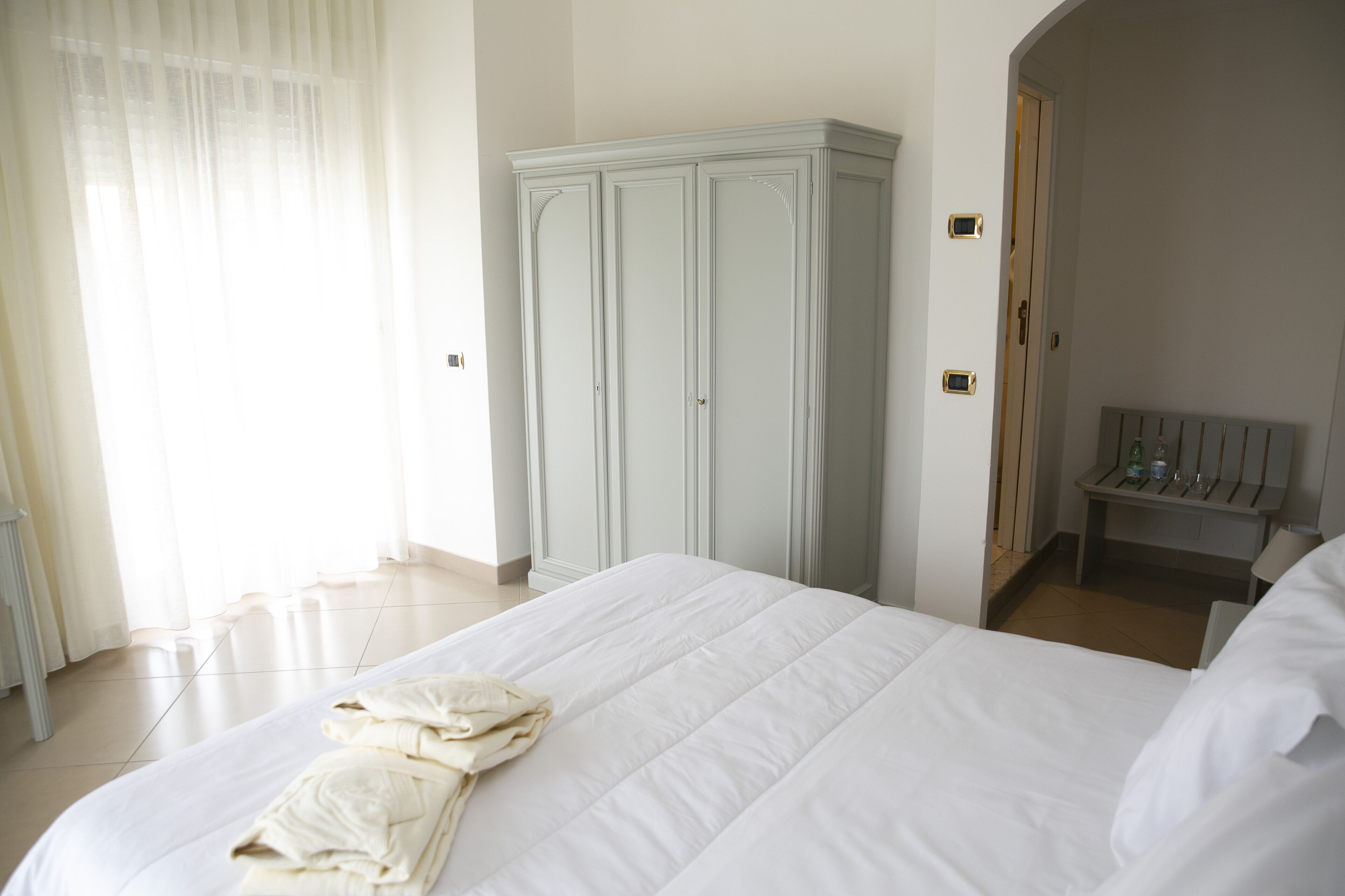 A hotel room with a large bed, a wardrobe, and a small table with a bottle and glasses.
