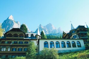 A traditional Alpine-style building with multiple windows and a steep roof, surrounded by lush greenery and mountains in the background. - Salegg (Castelrotto)